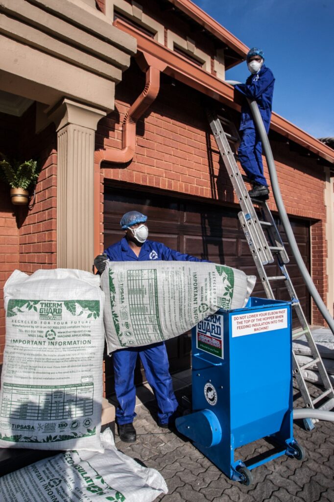 Thermguard installers feeding cellulose fibre insulation into the blowing machine at a home
